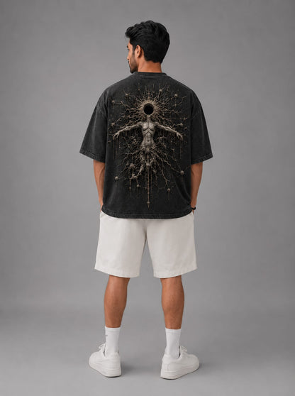 A model shown standing from the back against alight gray background, wearing a dark gray acid washed drop shoulder T-Shirt with a cosmic themed white body sculpture of an entity.