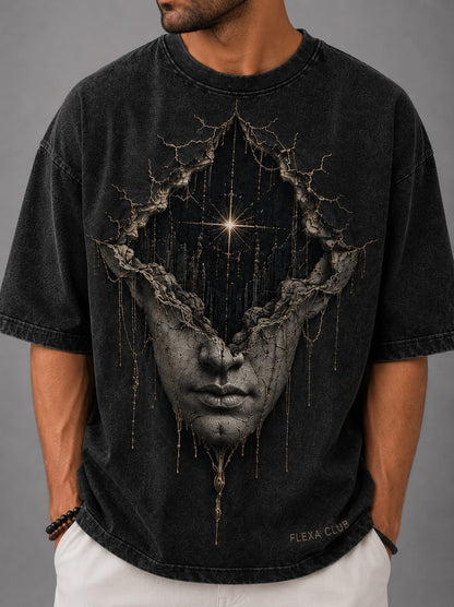A model shown against a light gray back ground, wearing a dark gray acid washed drop shoulder T-Shirt with a cosmic themed white sculpture of a face.