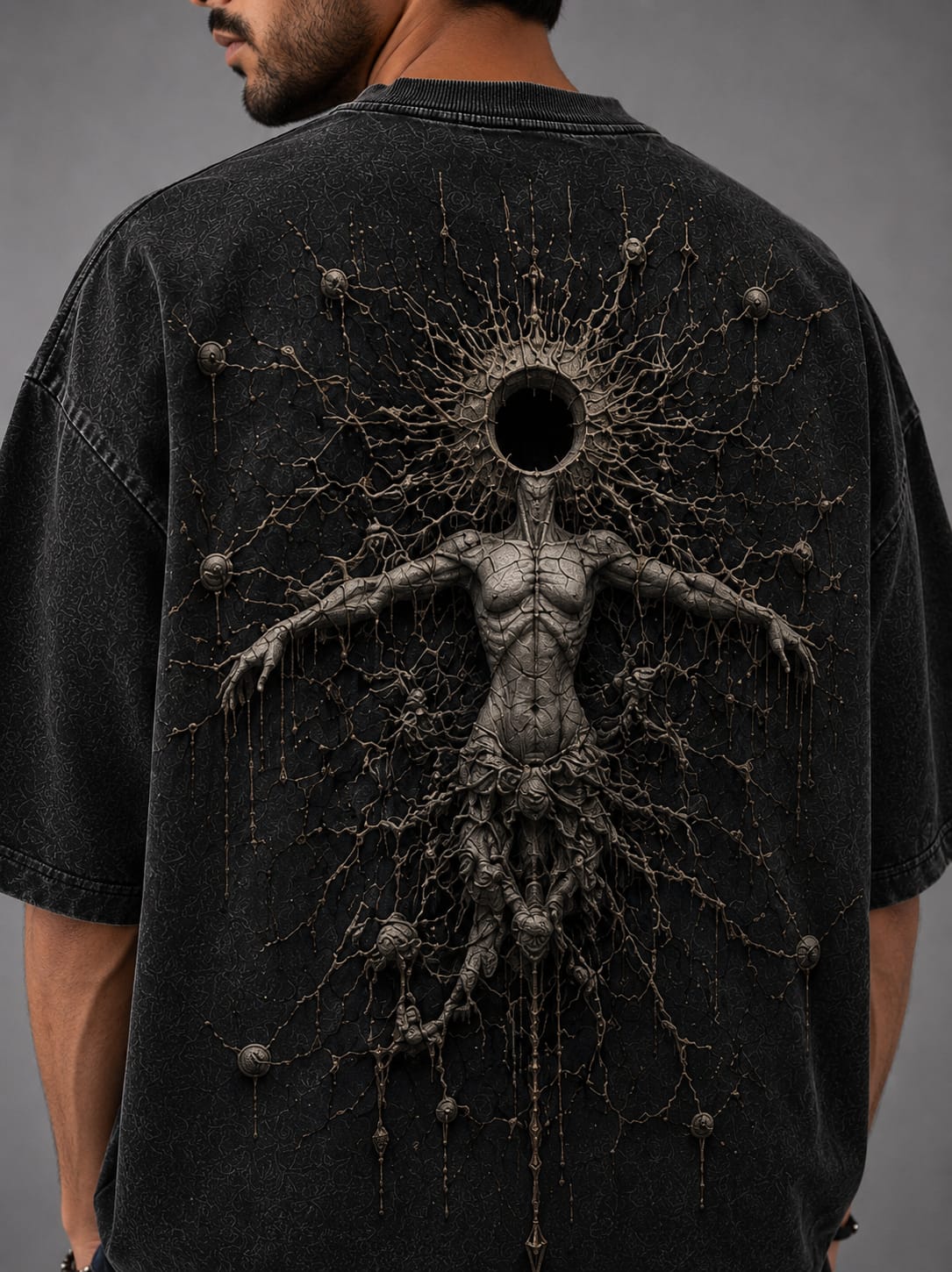 A model shown wearing a dark gray acid washed drop shoulder T-Shirt, against a light gray back ground with a cosmic themed sculpture of a cosmic entity.