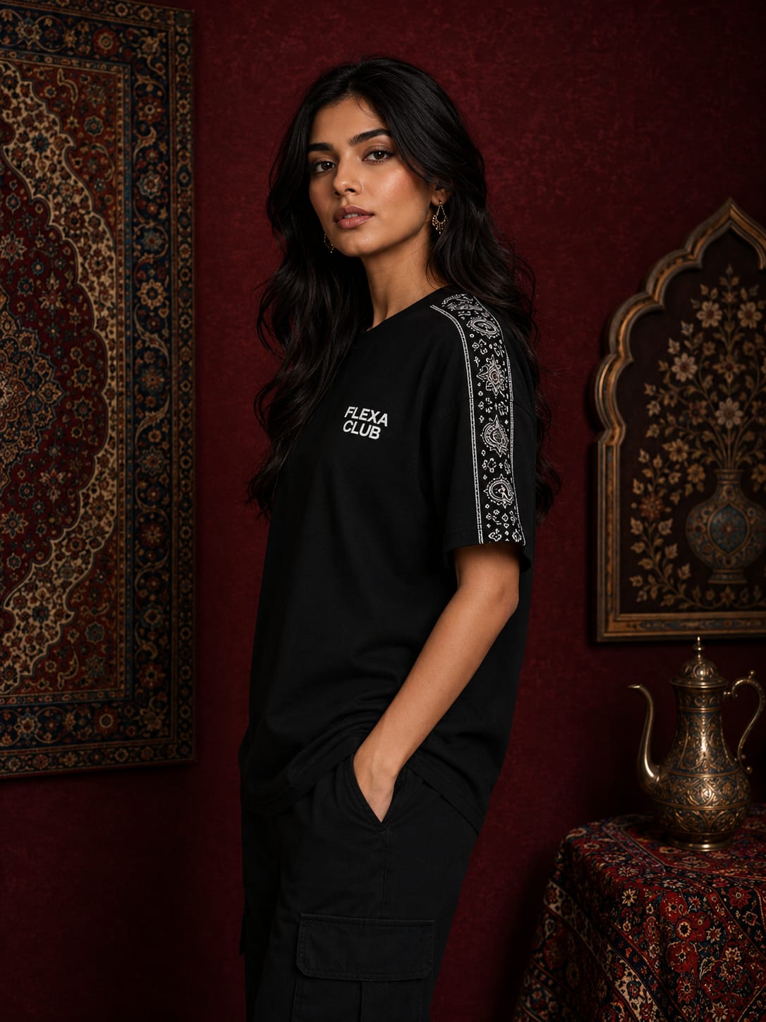 A woman wearing a black t-shirt with white 'FLEXA CLUB' text on the chest and a white patterned stripe down one sleeve, standing in a dark, ornate room with red walls and traditional decor.