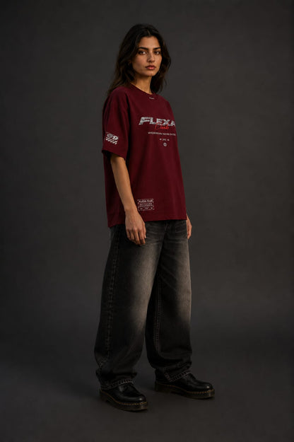 A woman wearing an oversized maroon t-shirt with 'FLEXA Club' racing graphics, against a dark gray studio background.