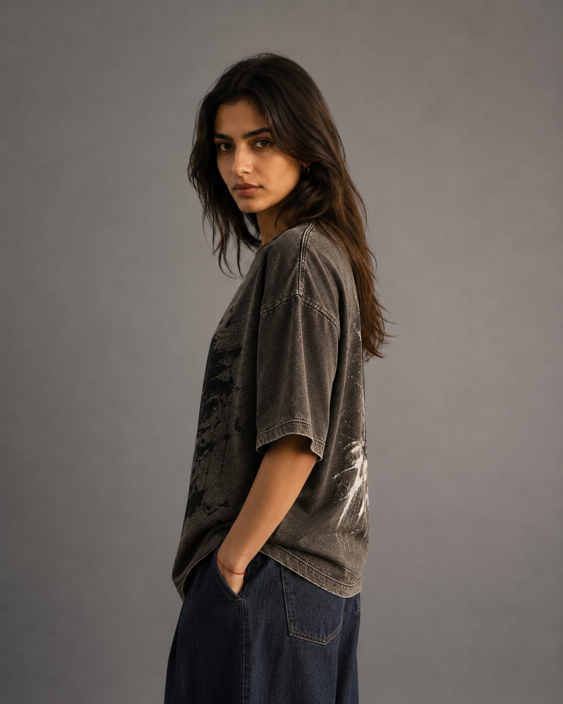 Woman wearing a dark gray t-shirt and blue jeans against a gray background